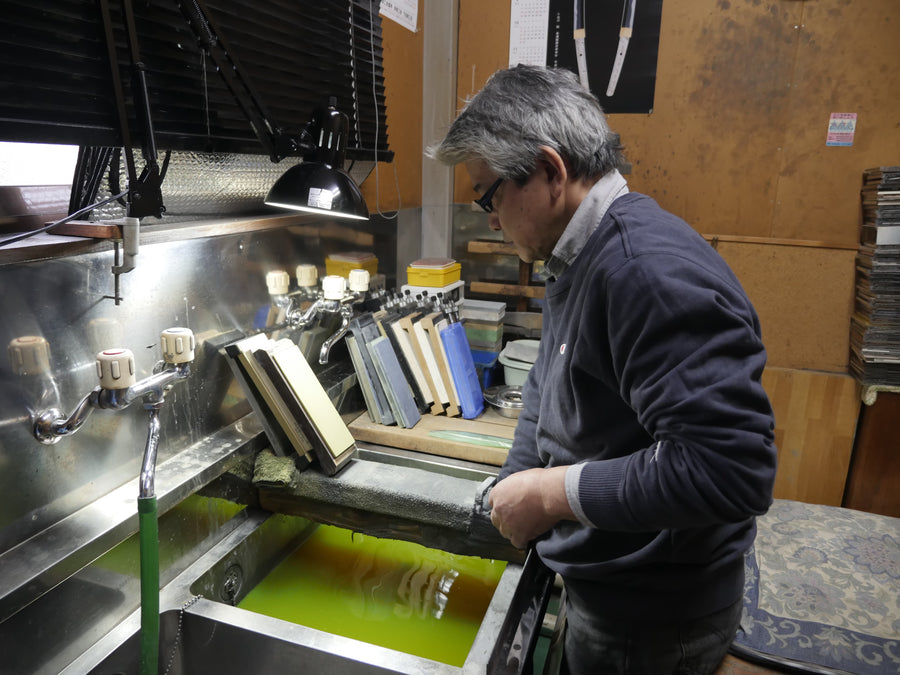 Tsukasa Hinoura sharpening a blade at his water station with whetstone rack, Sanjo, April 2016