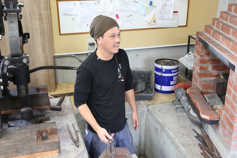 Yu Kurosaki holding tongs beside his power hammer in his Echizen forge