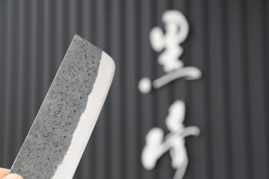 A tsuchime hammered-finish knife held up for display in Yu Kurosaki's Echizen workshop